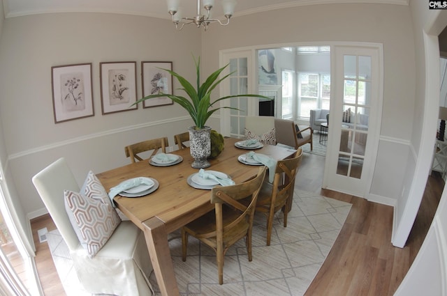 dining space with crown molding, light hardwood / wood-style floors, french doors, and a chandelier