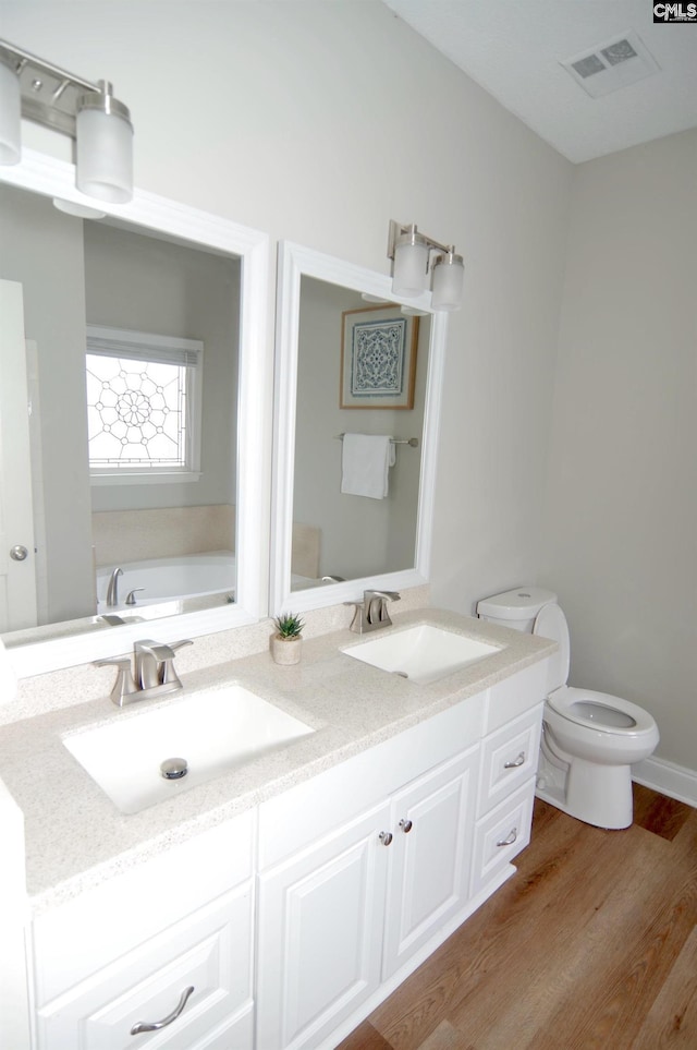 bathroom with hardwood / wood-style flooring, vanity, a tub, and toilet