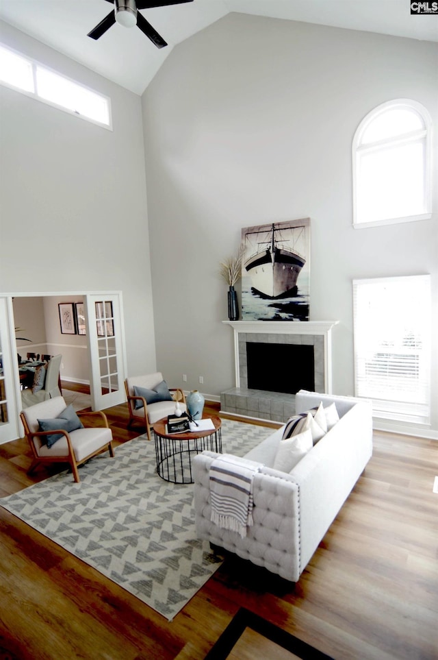 living room with ceiling fan, wood-type flooring, a tiled fireplace, and high vaulted ceiling