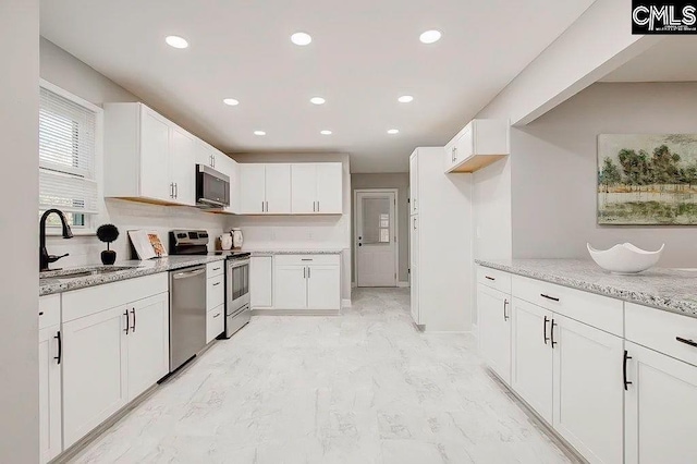 kitchen featuring stainless steel appliances, white cabinetry, light stone countertops, and sink