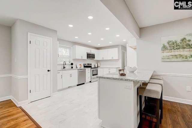 kitchen with sink, a breakfast bar area, appliances with stainless steel finishes, light stone countertops, and white cabinets