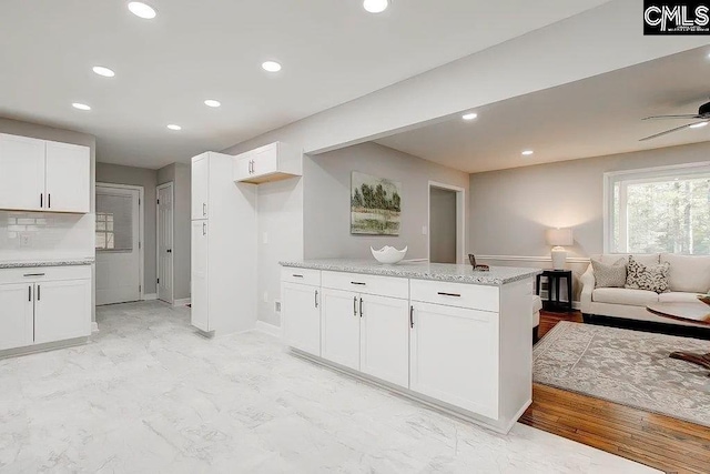 kitchen with tasteful backsplash, ceiling fan, white cabinets, and light stone counters