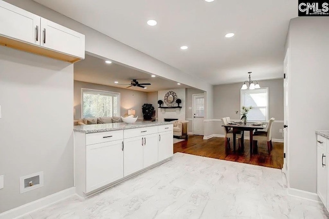 kitchen with white cabinetry, light stone counters, pendant lighting, and a healthy amount of sunlight