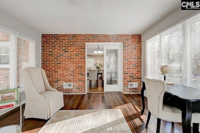 living area with brick wall, dark hardwood / wood-style flooring, and a chandelier