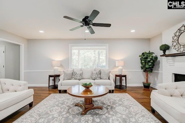 living room featuring ceiling fan, a brick fireplace, and dark hardwood / wood-style flooring