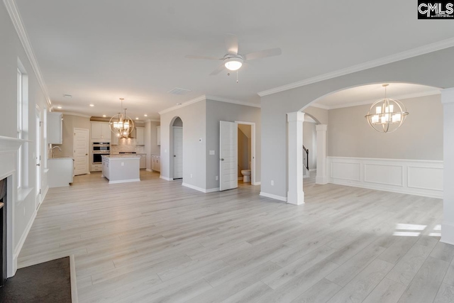 unfurnished living room featuring arched walkways, a fireplace, light wood finished floors, ornamental molding, and ceiling fan with notable chandelier