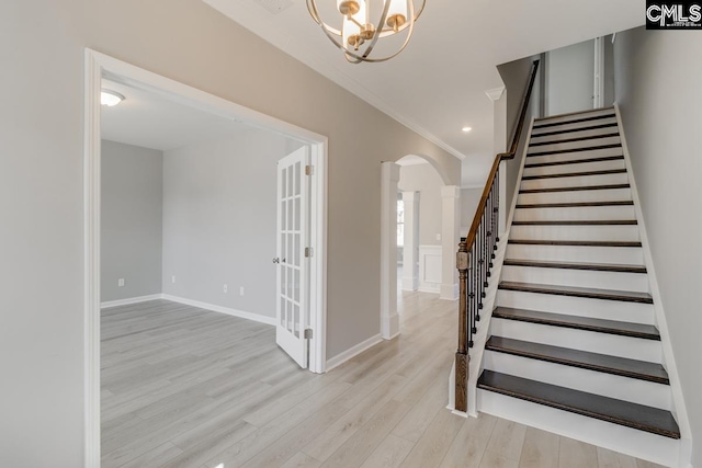 foyer entrance with arched walkways, stairway, light wood-style flooring, ornamental molding, and baseboards