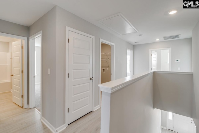 hall featuring light wood-type flooring, attic access, visible vents, and an upstairs landing