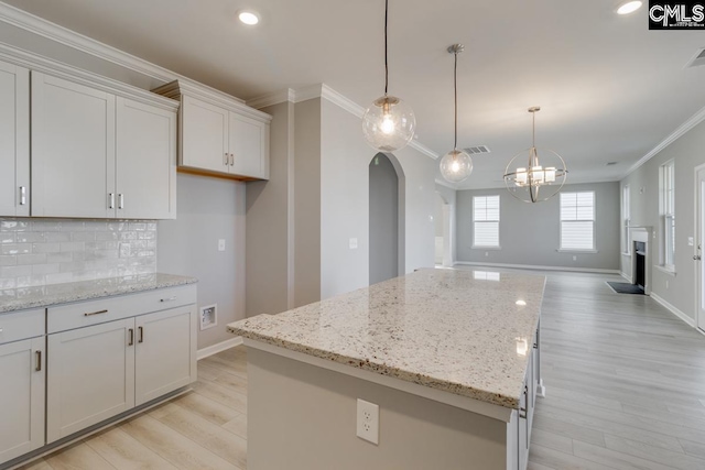 kitchen with arched walkways, a kitchen island, light wood-type flooring, tasteful backsplash, and crown molding