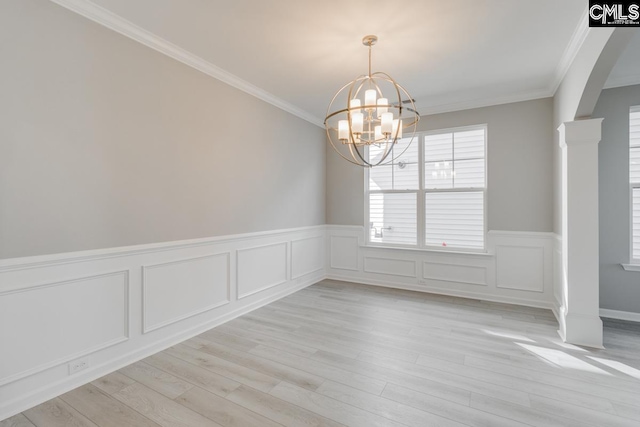 unfurnished dining area featuring decorative columns, arched walkways, ornamental molding, an inviting chandelier, and light wood-type flooring