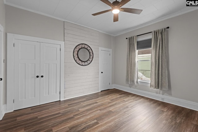 empty room with crown molding, ceiling fan, dark hardwood / wood-style flooring, and wood walls