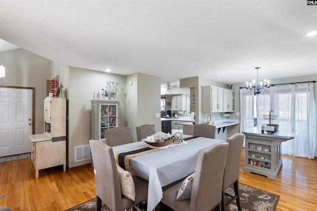 dining space with an inviting chandelier, a textured ceiling, and light wood-type flooring