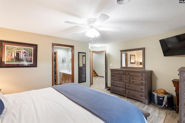 bedroom with ceiling fan, ensuite bathroom, a textured ceiling, and light wood-type flooring