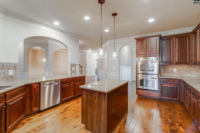 kitchen with light stone counters, tasteful backsplash, hanging light fixtures, light hardwood / wood-style flooring, and appliances with stainless steel finishes