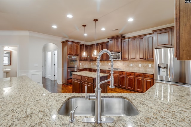 kitchen with sink, crown molding, hanging light fixtures, appliances with stainless steel finishes, and light stone countertops