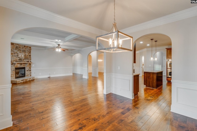 interior space with crown molding, a stone fireplace, dark hardwood / wood-style floors, and ceiling fan