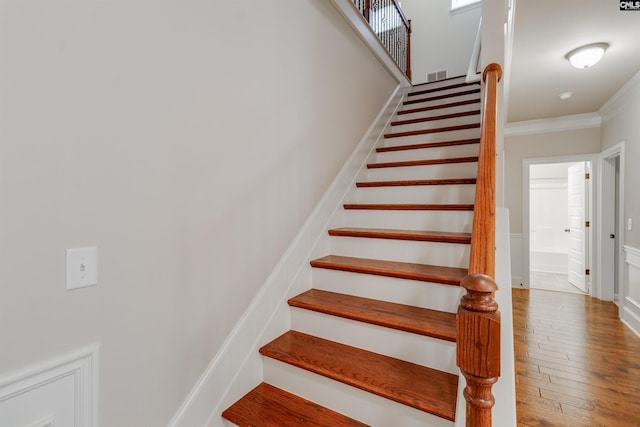 staircase with wood-type flooring and ornamental molding