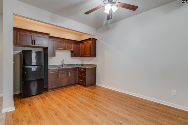 kitchen with light hardwood / wood-style flooring, ceiling fan, black refrigerator, dark brown cabinetry, and light stone countertops