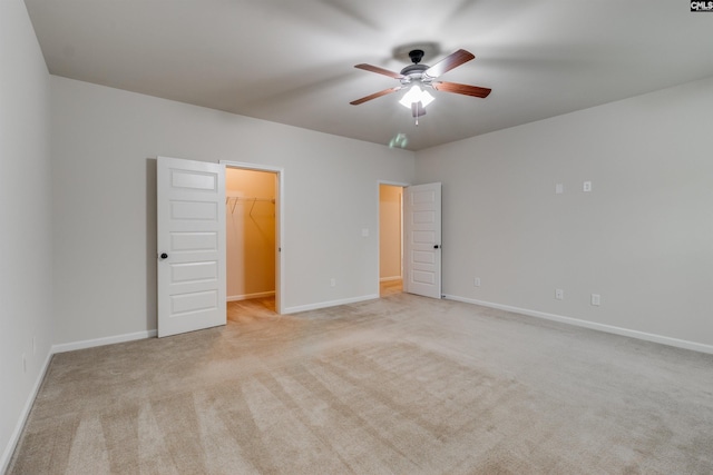 unfurnished bedroom with a spacious closet, light colored carpet, a closet, and ceiling fan