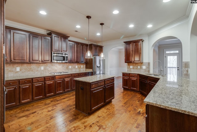 kitchen with sink, hanging light fixtures, stainless steel appliances, light stone countertops, and kitchen peninsula