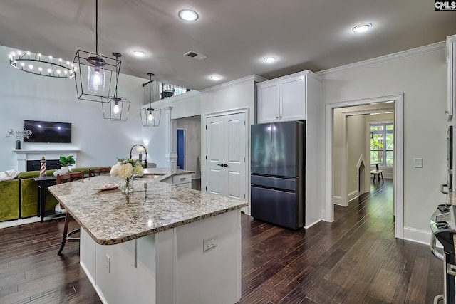 kitchen featuring a breakfast bar area, decorative light fixtures, refrigerator, an island with sink, and white cabinets