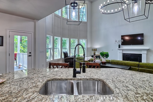 kitchen featuring ornamental molding, sink, light stone counters, and a towering ceiling