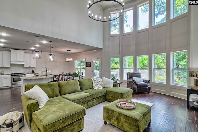 living room featuring dark hardwood / wood-style floors, sink, a notable chandelier, and a towering ceiling