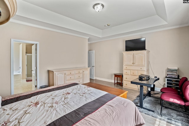 bedroom with crown molding, connected bathroom, light wood-type flooring, and a tray ceiling