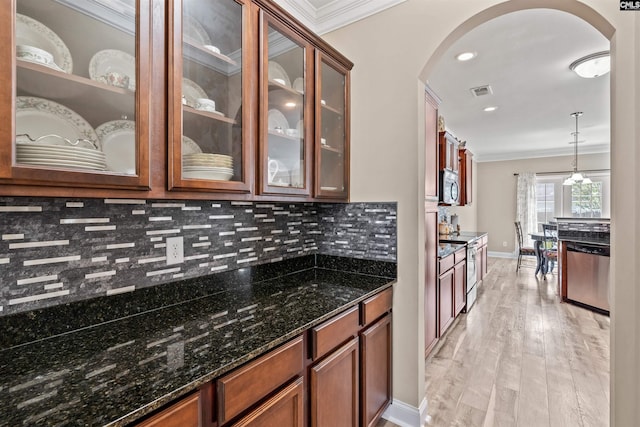 kitchen featuring hanging light fixtures, light wood-type flooring, ornamental molding, appliances with stainless steel finishes, and dark stone counters