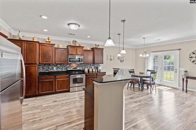 kitchen featuring pendant lighting, appliances with stainless steel finishes, backsplash, a kitchen island, and light wood-type flooring