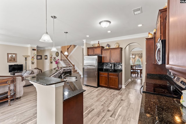 kitchen with light hardwood / wood-style flooring, hanging light fixtures, ornamental molding, appliances with stainless steel finishes, and dark stone counters