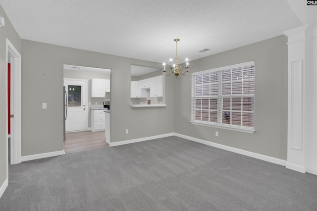 carpeted empty room featuring a notable chandelier and a textured ceiling