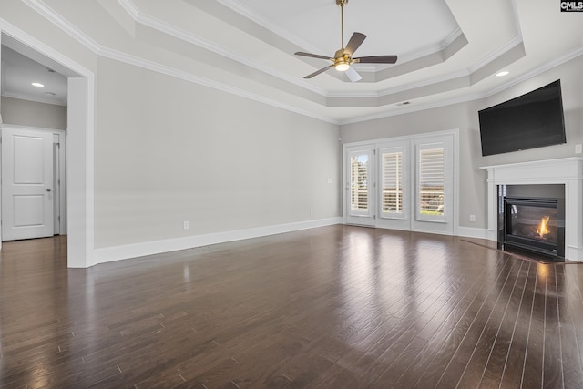 unfurnished living room featuring a raised ceiling, crown molding, dark wood-type flooring, and ceiling fan