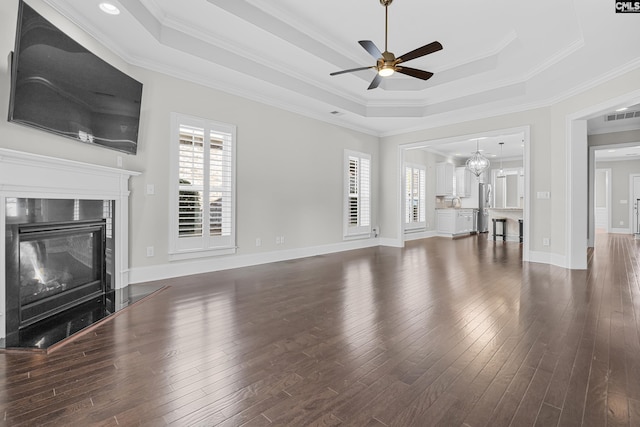 unfurnished living room with dark wood-type flooring, a premium fireplace, a raised ceiling, and ceiling fan with notable chandelier