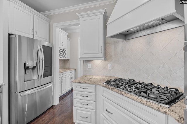 kitchen with premium range hood, appliances with stainless steel finishes, white cabinetry, ornamental molding, and light stone countertops