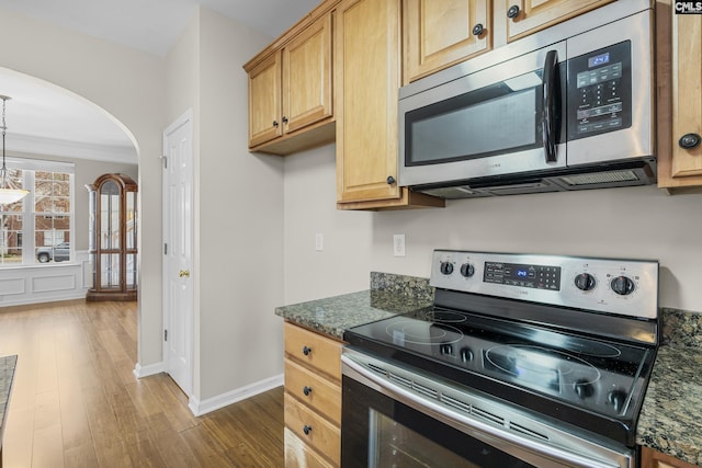 kitchen featuring dark stone countertops, stainless steel appliances, hanging light fixtures, and light wood-type flooring