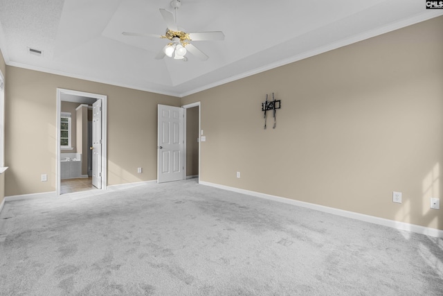 unfurnished bedroom featuring ensuite bathroom, crown molding, a tray ceiling, ceiling fan, and carpet