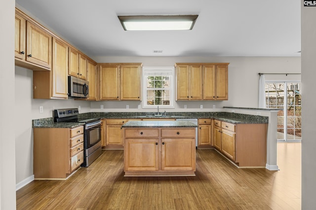 kitchen featuring sink, a center island, light hardwood / wood-style flooring, appliances with stainless steel finishes, and dark stone counters