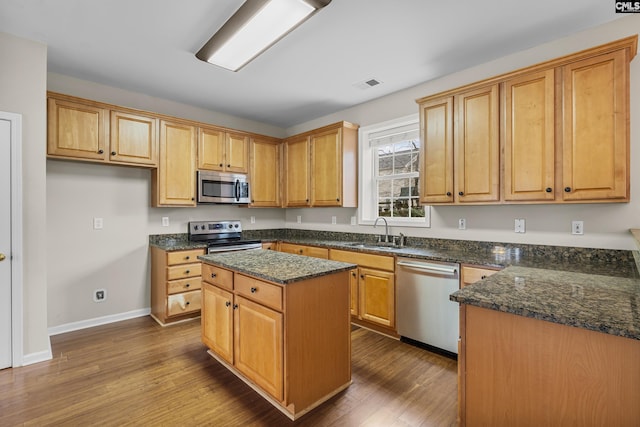 kitchen with sink, dark wood-type flooring, stainless steel appliances, a center island, and dark stone counters