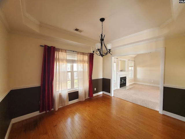 unfurnished living room with a raised ceiling, ornamental molding, hardwood / wood-style floors, and a chandelier