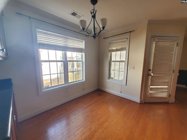 unfurnished dining area featuring wood-type flooring, ornamental molding, and an inviting chandelier