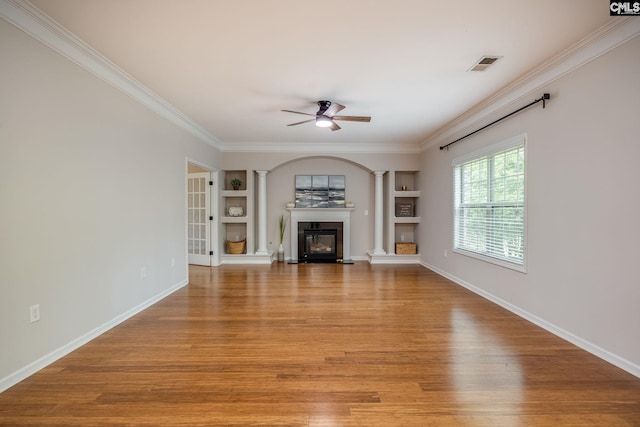 unfurnished living room with ornate columns, crown molding, light wood-type flooring, and built in shelves