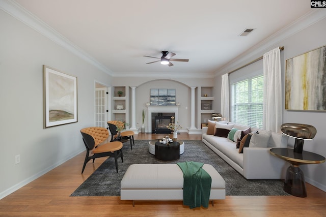 living room with built in shelves, crown molding, hardwood / wood-style floors, and ornate columns