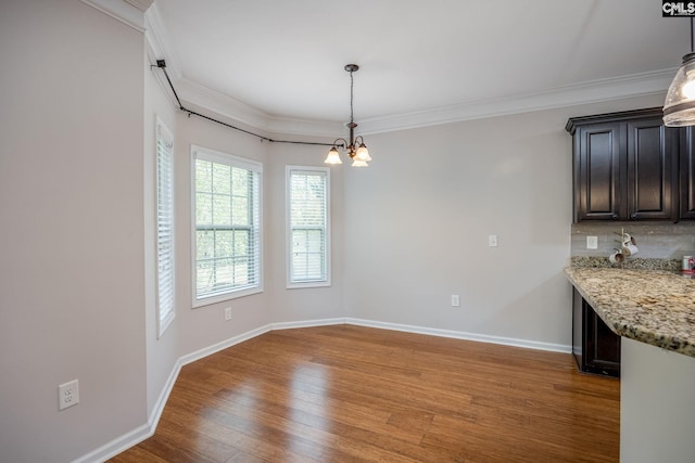 unfurnished dining area featuring wood-type flooring, ornamental molding, and an inviting chandelier