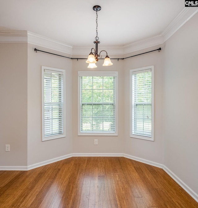 spare room featuring crown molding, a notable chandelier, hardwood / wood-style flooring, and a wealth of natural light