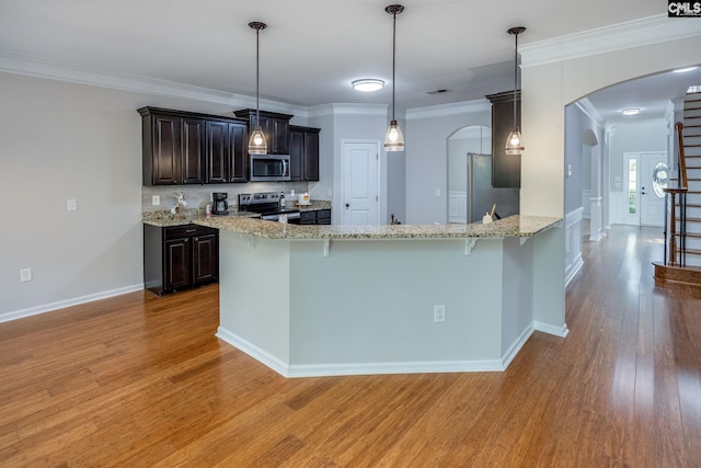 kitchen featuring appliances with stainless steel finishes, a kitchen breakfast bar, ornamental molding, light hardwood / wood-style floors, and dark brown cabinets