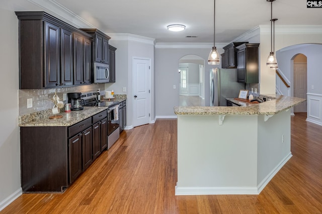 kitchen with dark brown cabinets, appliances with stainless steel finishes, a breakfast bar, and hanging light fixtures