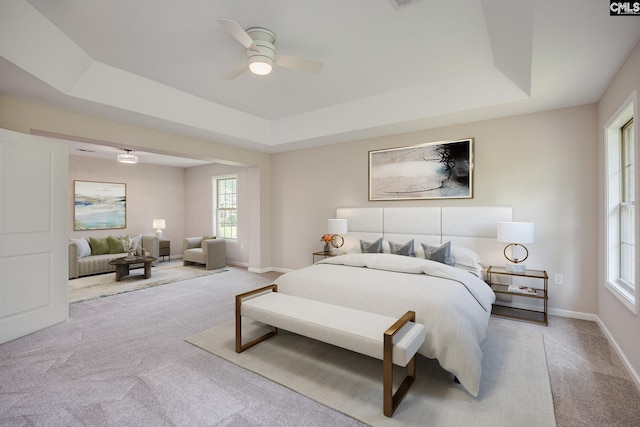 bedroom featuring multiple windows, light colored carpet, and a tray ceiling