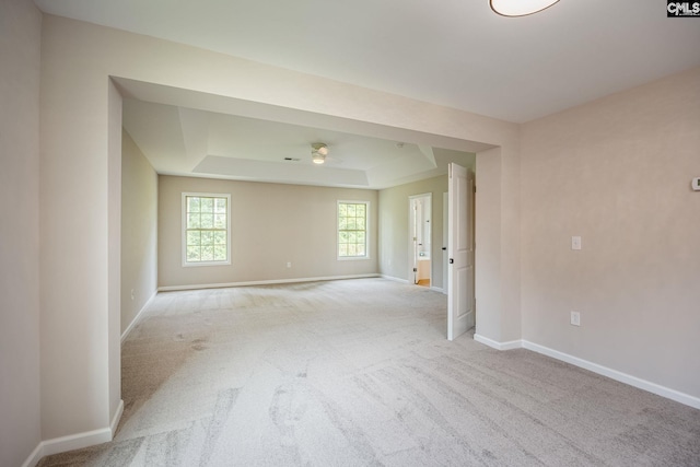 spare room featuring a raised ceiling, light colored carpet, and ceiling fan