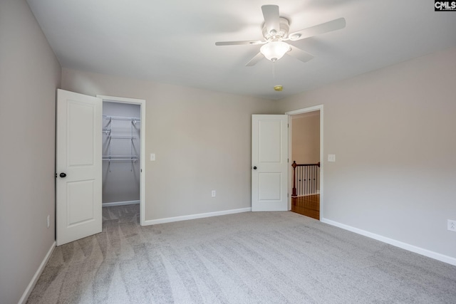 unfurnished bedroom with a spacious closet, light colored carpet, ceiling fan, and a closet